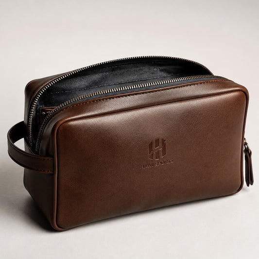 Brown leather toiletry bag with open zipper, dark interior, side handle and embossed Hawi Sports logo